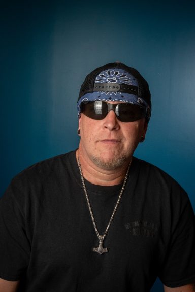 Headshot of rocker dude with bandana and sunglasses against a teal backdrop