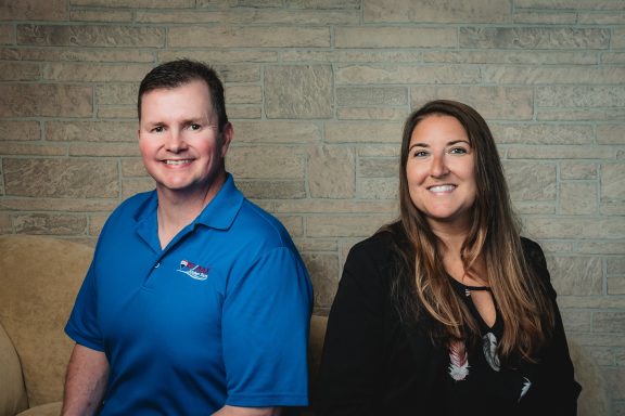 Headshot of a man and woman with tan brick background