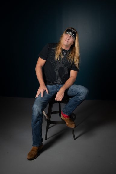 Full body shot of long hair rocker dude sitting on stool