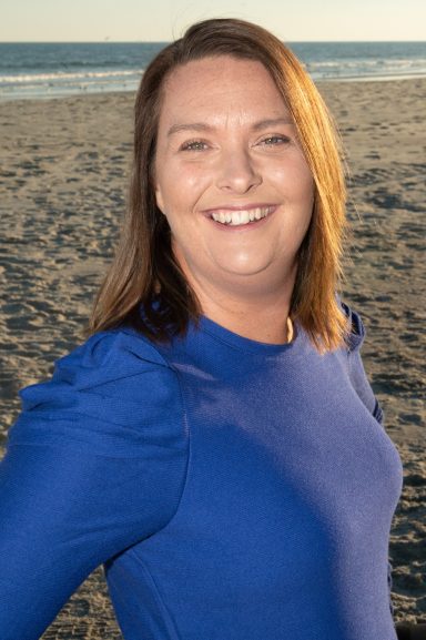 Headshot of a woman in a blue shirt on the beach at sunset