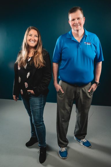 Full body shot of a man and woman against a teal wall and grey floor